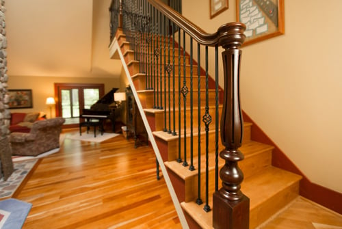Iron Balusters and polished wooden newel on light colored wooden stairs