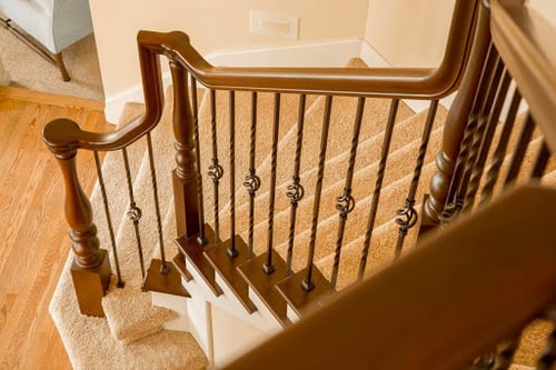 unique wood handrail with gooseneck fitting over twisted basket iron balusters on carpeted stairs